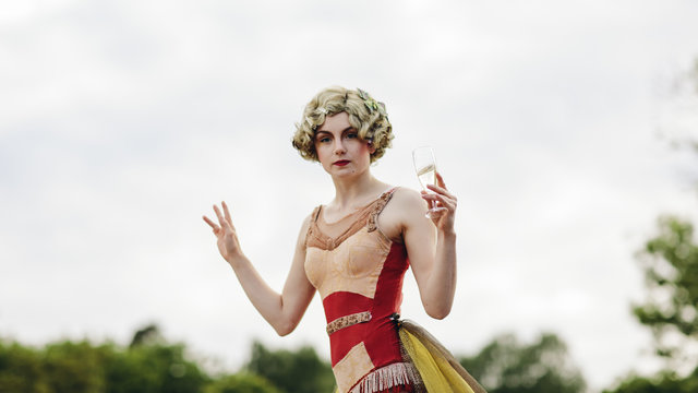 Portrait of young acrobat woman holding glass of champagne outdoors