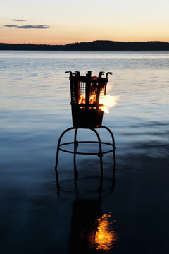 Sweden, Stockholm, Sodermanland, Dalaro, Brazier on lake at sunset