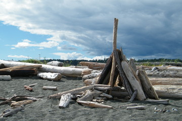 Driftwood Teepee on a Sandy Beach with Clouds Blowing Away