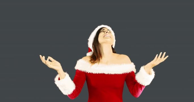 Joyful santa girl looking up and smiling at camera on grey background