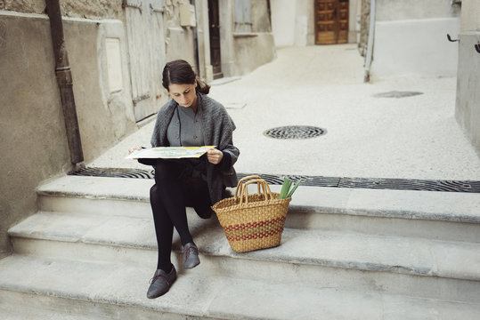Young woman sitting on steps and looking at map outdoors