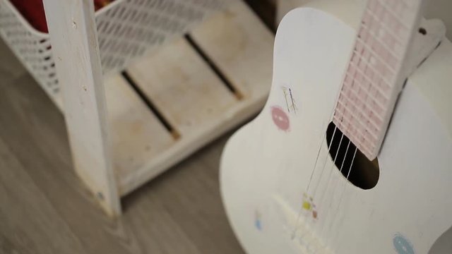 Old acoustic guitar painted in white stands in corner of art studio