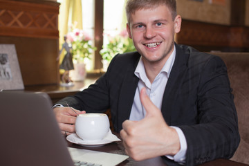 Business, technology. Young man working on a laptop with a mug o