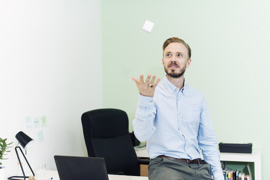 Sweden, Businessman throwing up white cube in office