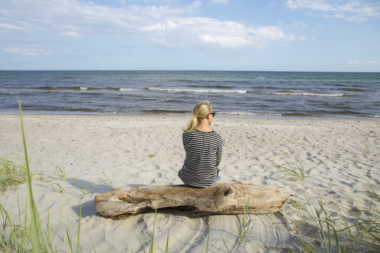 Rear view of woman sitting on wooden log at beach