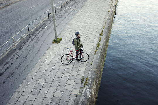 Thoughtful man with bicycle standing on bridge