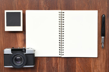 Blank notebook with pen, photo frames and camera on wooden background.