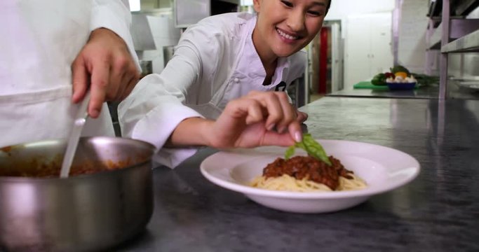Chef serving up spaghetti and another garnishing with basil leaf