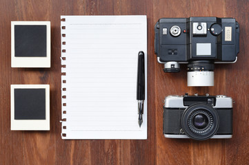Blank paper with pen, photo frames and camera on wooden background.