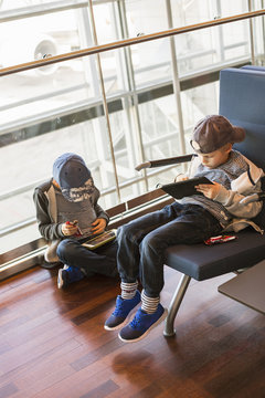 Sweden, Uppland, Two boys (6-7, 8-9) sitting and playing with tablets at waiting area of Arlanda Airport