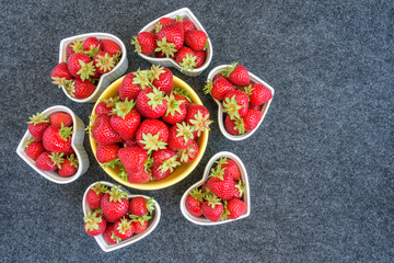Fresh picked strawberries in a yellow bowl, and white heart shaped bowls, on a gray background
