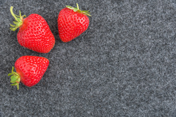 Three fresh picked strawberries on a gray background
