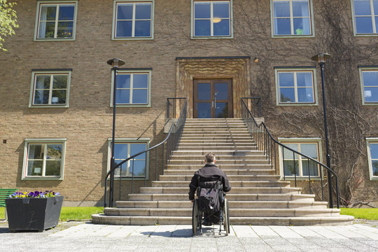 Rear view of man sitting in wheelchair in front of stairs