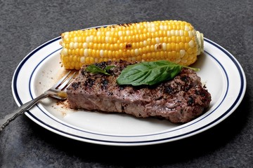 Meat and corn grilled on plate.