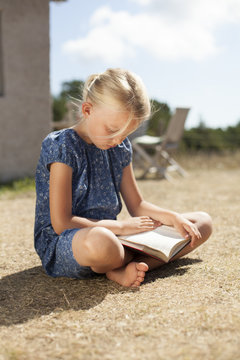 Girl reading book while sitting in backyard