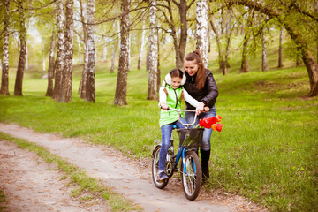 Fototapeta premium happy mother teaches his daughter to ride a bike. Mother holds daughter from falling