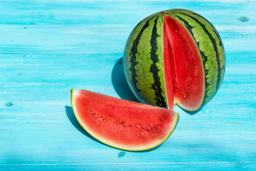 Fresh watermelon with one section sliced on blue wooden background