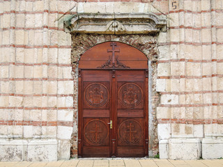 Church door.  Entrance wooden door of the old Orthodox Church decorated with carvings on the background of stone facade wall