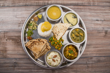 typical maharashtrian food served in a steal plate, marathi food includes kadhi and shrikhand, plain dal, spinach curry, aalu mutter, plain rice, papad, bhakri or bhakar or roti and variety of salad © StockImageFactory
