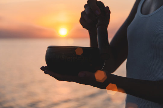 Practice With Singing Bowl At The Beach At Sunset. Lens Flare Effect