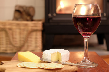 Cosy evening at home with red wine, brie or camembert cheese and crackers, in front of a fire in a woodburner or wood burning stove.