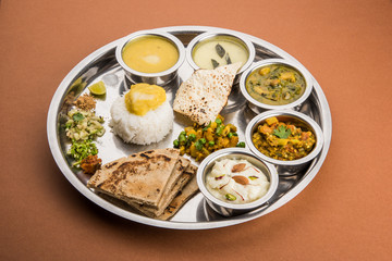 typical maharashtrian food served in a steal plate, marathi food includes kadhi and shrikhand, plain dal, spinach curry, aalu mutter, plain rice, papad, bhakri or bhakar or roti and variety of salad © StockImageFactory