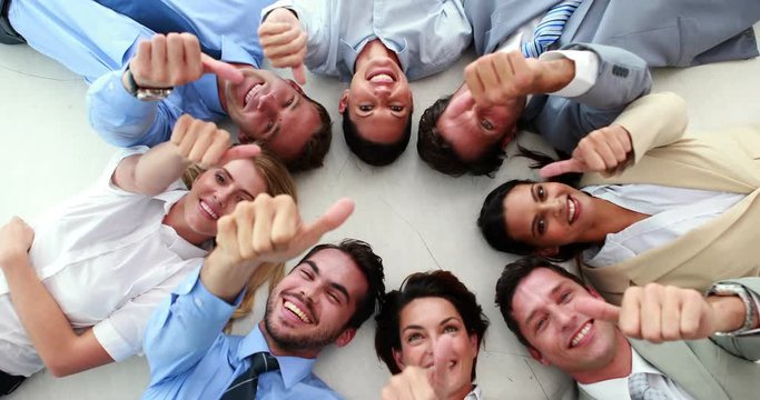 Business people lying in a circle showing thumbs up in the office