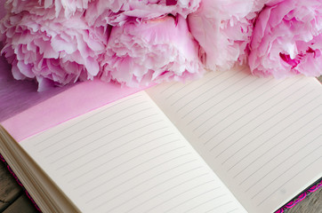 Open notebook for notes next to blooming pink peonies