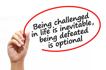 Man writing Being challenged in life is inevitable,being defeated is optional with marker on transparent wipe board.