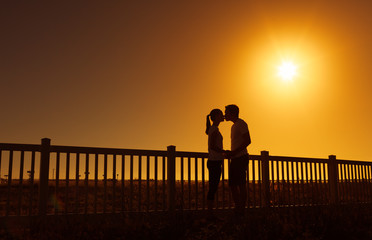 Young couple kissing against a bright sunset. 