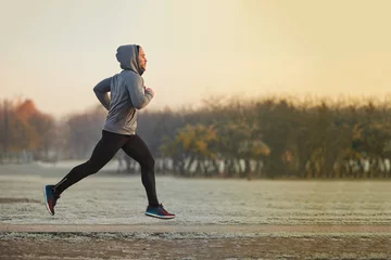 Poster Im Rahmen Junger athletischer Mann, der während des kalten Herbstmorgens im Park läuft © baranq