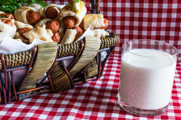 Wicker basket with mini artisan hot dogs (Sausage in the dough) and a glass of fresh cow's milk of the village, on a plaid background