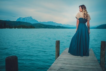 Well-dressed woman sitting on the wooden pier with mountain river view.