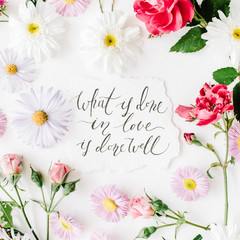 inspirational quote "what is done in love is done well" written in calligraphy style on paper with pink, red roses, chamomiles and leaves isolated on white background. Flat lay, top view