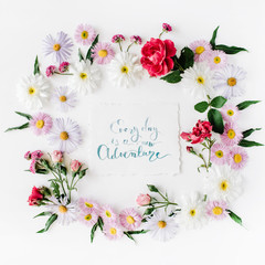 inspirational quote "everyday is a new adventure" written in calligraphy style on paper with pink, red roses, chamomiles and leaves isolated on white background. Flat lay, top view