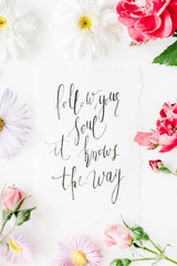 inspirational quote "follow your soul it knows the way" written in calligraphy style on paper with pink, red roses, chamomiles and leaves isolated on white background. Flat lay, top view