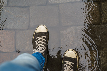 Male legs in sneakers walking through rain puddle