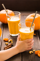 Children's hand hold a glass of pumpkin spiced smoothies on a dark wooden background