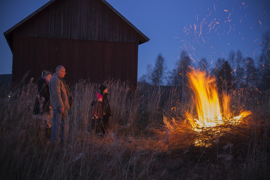 Family Looking At Bonfire While Standing Outdoors At Night