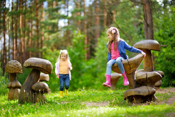 Two cute little sisters having fun on giant wooden mushrooms