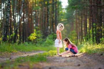 Two adorable little sisters hiking in a forest on summer