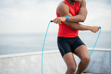 Detail of male runner jumping rope for warming up. Black sporty man training and exercising outside.