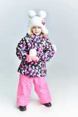 Cute little funny child in colorful winter clothes having fun with snow, outdoors during snowfall. Active outdoors leisure with children in winter. Kid with  hat, hand gloves with stripes.