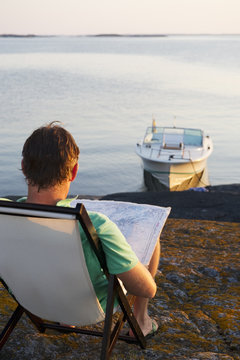 Sweden, Sodermanland, Stockholm Archipelago, Varmdo, Rear view of mature man on lounge chair reading map on rocky beach