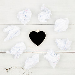 crumpled paper around a small blackboard in form of heart on white wooden table