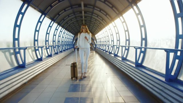 Stylish business woman dressed in white comes with travel bag on the tunnel of glass or transition. Light of the setting sun, enjoys a telephone.