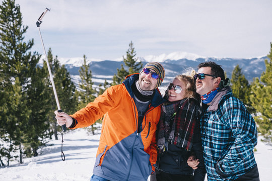 Three people, two men and a young woman in skiing gear posing for a selfie, one holding a selfie stick. 