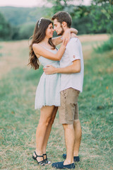 Fototapeta premium Beautiful young couple lovingly look at each other and embracing on the green meadow. Back view. Wonderful summer day