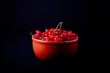 Currant berries in a clay bowl on black background. Selective fo