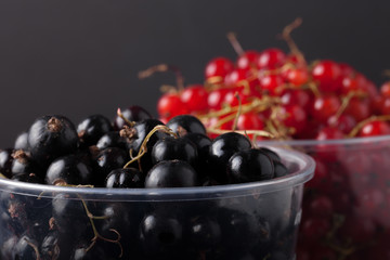 Currant berries in a plastic glass on black background. Selectiv